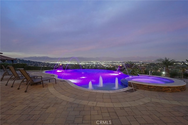 pool at dusk featuring a patio area, an in ground hot tub, pool water feature, and a mountain view