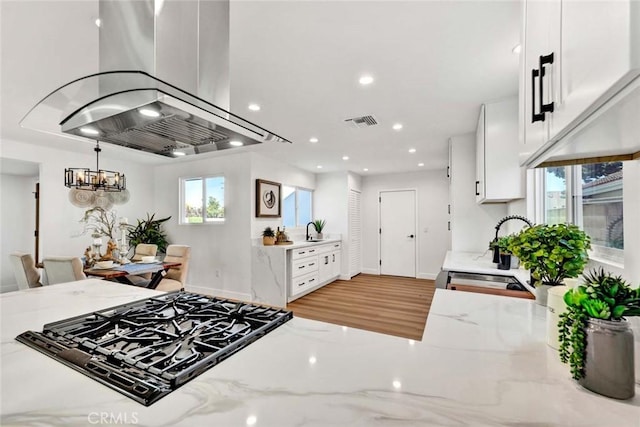 kitchen with a healthy amount of sunlight, white cabinetry, island exhaust hood, and light stone countertops