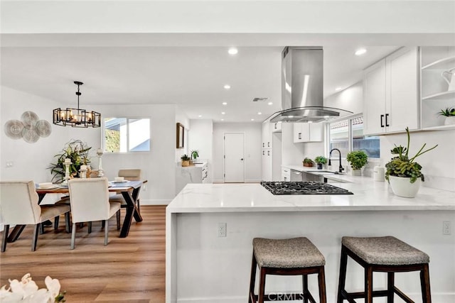 kitchen featuring sink, white cabinetry, kitchen peninsula, stainless steel gas stovetop, and island range hood