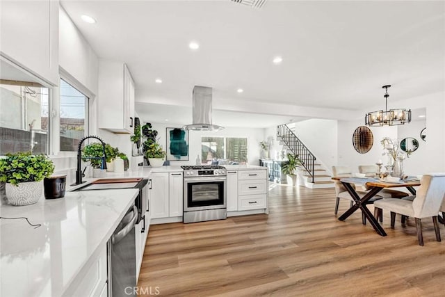 kitchen with appliances with stainless steel finishes, white cabinetry, island range hood, and a wealth of natural light