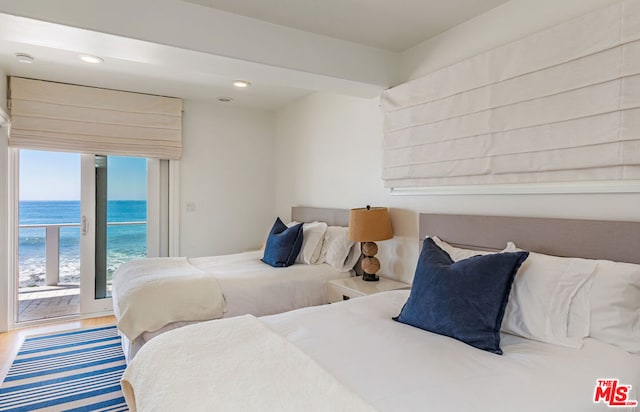 bedroom with access to exterior, wood-type flooring, a water view, and a beach view