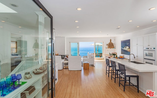 kitchen featuring sink, pendant lighting, a water view, light hardwood / wood-style flooring, and white cabinetry