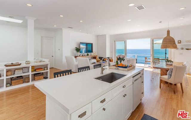 kitchen featuring a kitchen island with sink, white dishwasher, sink, light wood-type flooring, and white cabinetry