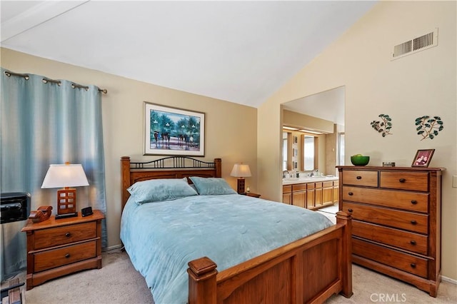 bedroom featuring ensuite bathroom, light colored carpet, and lofted ceiling