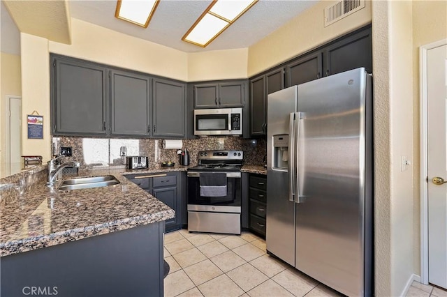 kitchen featuring appliances with stainless steel finishes, backsplash, sink, light tile patterned floors, and dark stone countertops