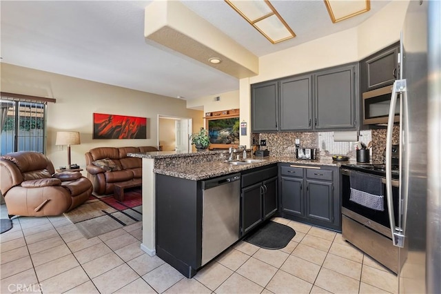 kitchen featuring dark stone countertops, light tile patterned floors, appliances with stainless steel finishes, tasteful backsplash, and kitchen peninsula