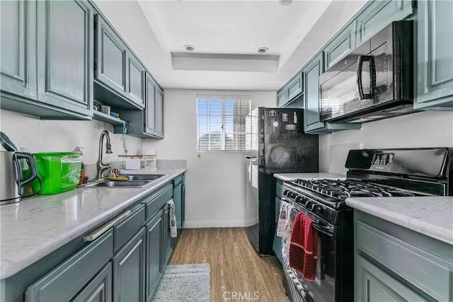 kitchen with sink, light stone counters, light hardwood / wood-style flooring, a tray ceiling, and black appliances