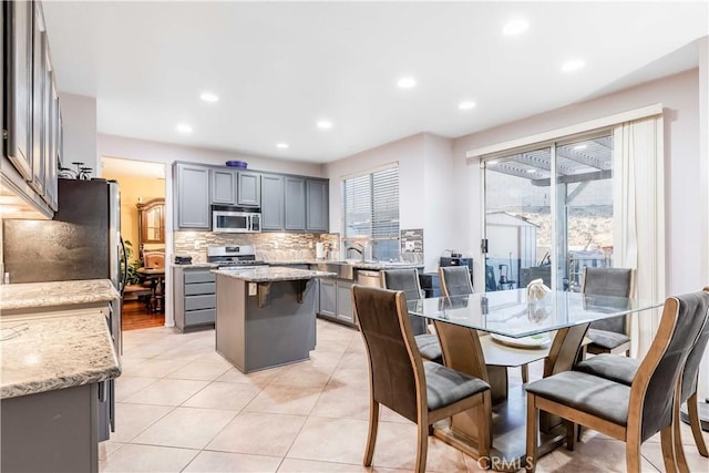 kitchen featuring light stone countertops, stainless steel appliances, a kitchen island, and gray cabinetry