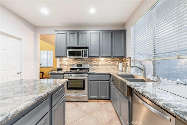 kitchen with light stone countertops, gray cabinetry, stainless steel appliances, sink, and light tile patterned floors