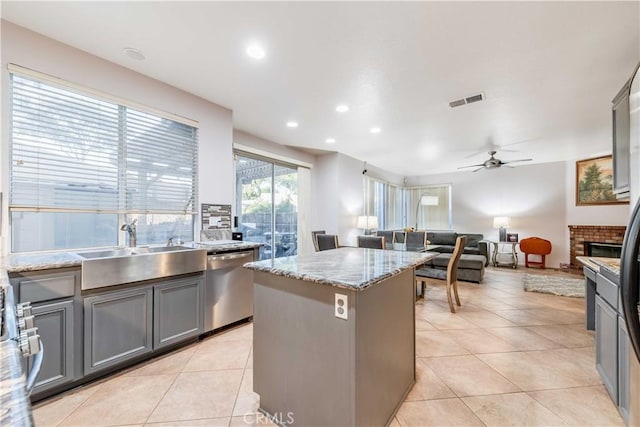 kitchen with gray cabinetry, a center island, a brick fireplace, stainless steel dishwasher, and ceiling fan