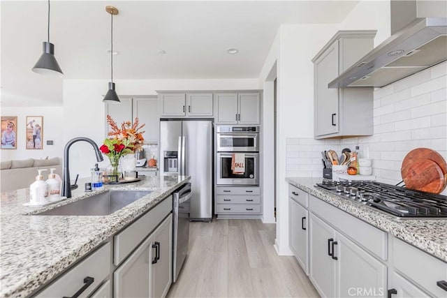 kitchen featuring sink, hanging light fixtures, stainless steel appliances, wall chimney range hood, and backsplash