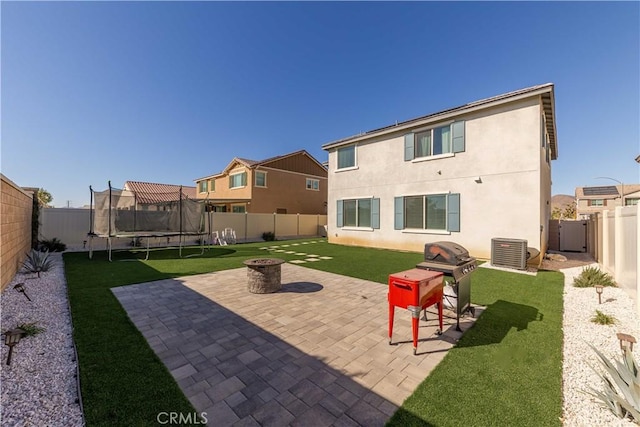 rear view of house with a lawn, a fire pit, a trampoline, cooling unit, and a patio area