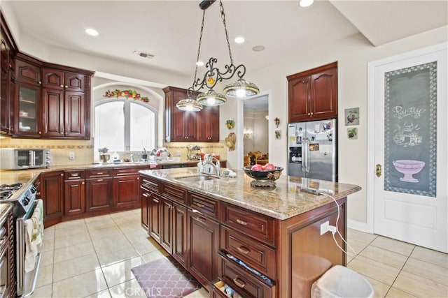 kitchen with a center island with sink, sink, appliances with stainless steel finishes, decorative light fixtures, and light tile patterned flooring