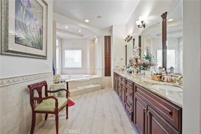 bathroom with hardwood / wood-style floors, vanity, and tiled tub