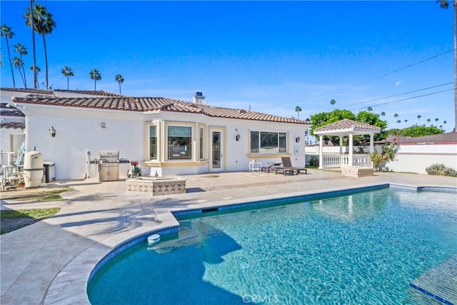 rear view of property featuring a gazebo, a fire pit, a patio area, and a fenced in pool