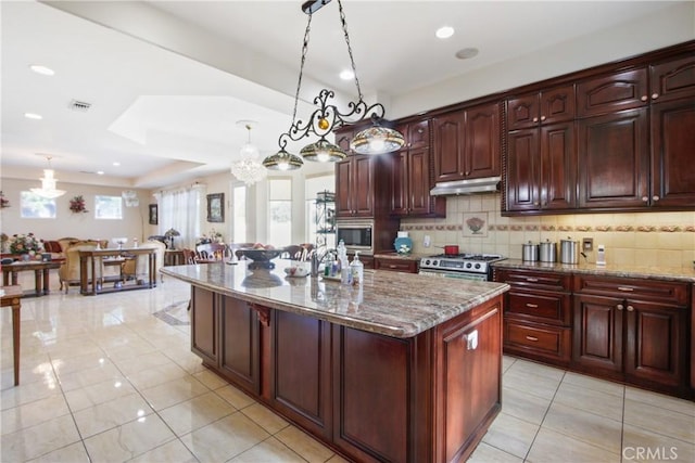 kitchen with light stone counters, an island with sink, decorative light fixtures, decorative backsplash, and appliances with stainless steel finishes