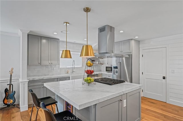 kitchen featuring light stone countertops, appliances with stainless steel finishes, island range hood, sink, and decorative light fixtures