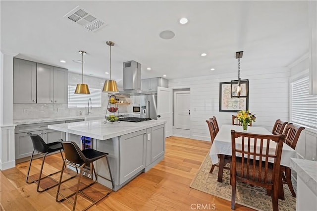 kitchen with a center island, hanging light fixtures, island exhaust hood, gray cabinets, and light wood-type flooring