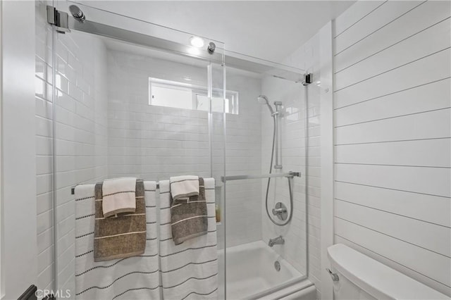 bathroom with shower / bath combination with glass door, wooden walls, and toilet