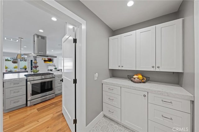 kitchen with stainless steel gas range, light hardwood / wood-style floors, light stone counters, white cabinetry, and island exhaust hood