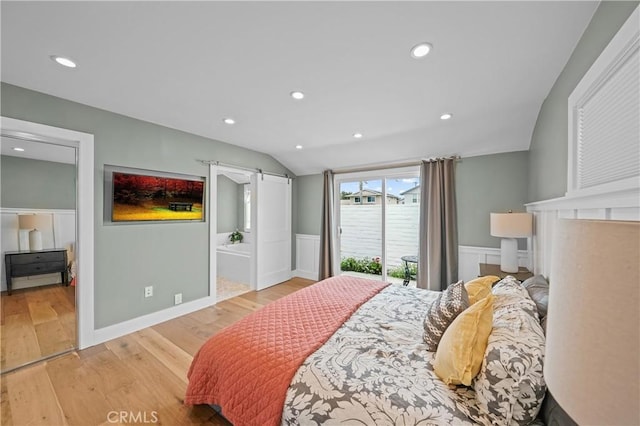 bedroom with connected bathroom, a barn door, light hardwood / wood-style flooring, lofted ceiling, and access to outside