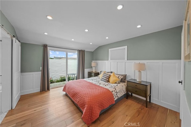 bedroom with a barn door, vaulted ceiling, access to outside, and light hardwood / wood-style flooring