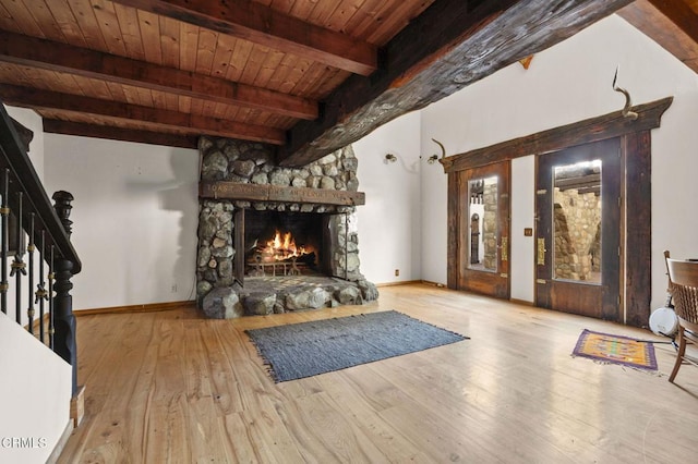 unfurnished room with beamed ceiling, light hardwood / wood-style floors, wooden ceiling, and a stone fireplace