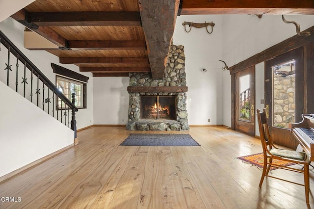 unfurnished living room featuring wood ceiling, light hardwood / wood-style floors, beam ceiling, and a stone fireplace