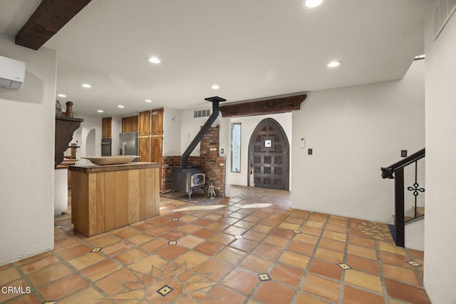 interior space featuring beam ceiling, an AC wall unit, a wood stove, and tile patterned floors