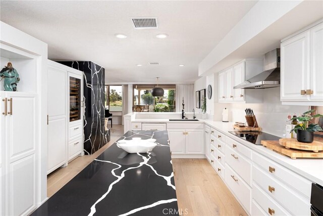 kitchen with wall chimney exhaust hood, white cabinetry, sink, and decorative light fixtures