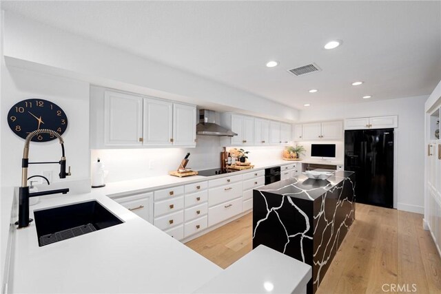 kitchen featuring wall chimney range hood, white cabinets, light hardwood / wood-style floors, and black appliances