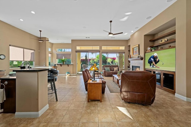 tiled living room with ceiling fan, sink, and a tile fireplace