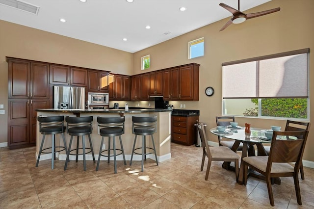 kitchen featuring ceiling fan, a breakfast bar, light tile patterned floors, a center island with sink, and appliances with stainless steel finishes