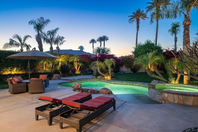 pool at dusk with a patio area and an in ground hot tub