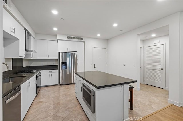 kitchen featuring appliances with stainless steel finishes, wall chimney exhaust hood, sink, white cabinets, and a breakfast bar area