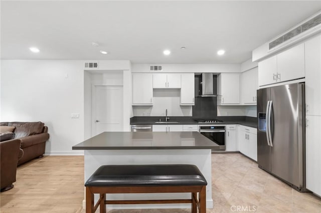 kitchen with stainless steel appliances, a kitchen island, sink, wall chimney range hood, and white cabinetry