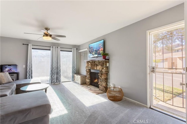 carpeted living room with ceiling fan, a wealth of natural light, and a stone fireplace