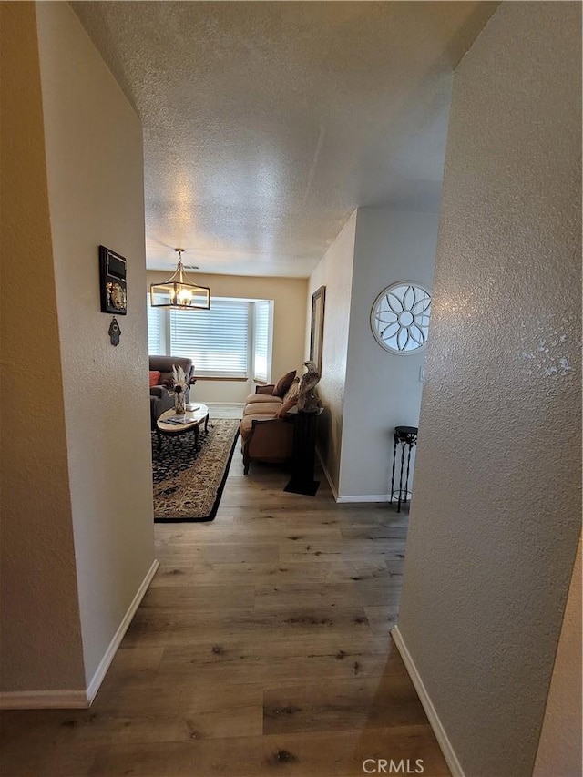 hallway featuring a textured ceiling, hardwood / wood-style flooring, and a notable chandelier