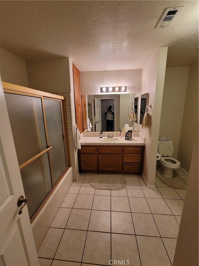 full bathroom with tile patterned floors, bath / shower combo with glass door, a textured ceiling, toilet, and vanity