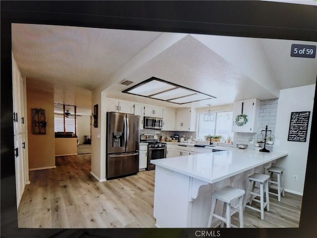 kitchen with white cabinets, stainless steel appliances, kitchen peninsula, and tasteful backsplash