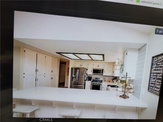 kitchen featuring backsplash, a kitchen breakfast bar, kitchen peninsula, white cabinetry, and stainless steel appliances