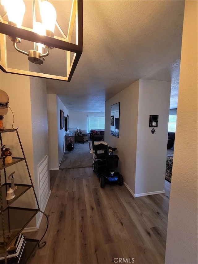 corridor with hardwood / wood-style flooring, a notable chandelier, and a textured ceiling