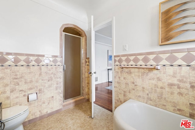 bathroom featuring a tub to relax in, toilet, and tile walls