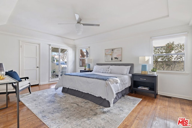 bedroom with hardwood / wood-style floors, access to exterior, ceiling fan, and a tray ceiling