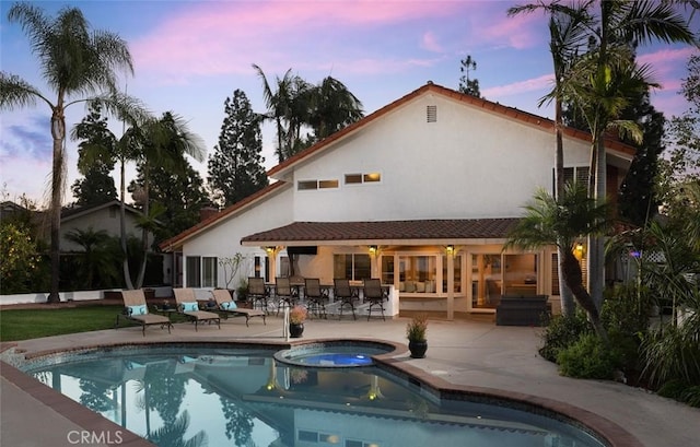 back house at dusk with a swimming pool with hot tub and a patio area