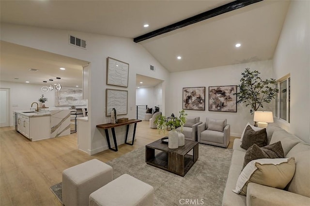 living room with light hardwood / wood-style floors, vaulted ceiling with beams, and sink