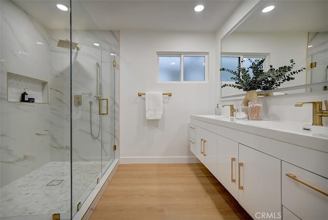 bathroom with double vanity, a marble finish shower, wood finished floors, a sink, and recessed lighting