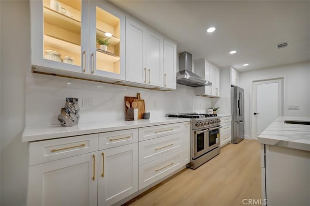 kitchen featuring wall chimney range hood, high end appliances, glass insert cabinets, and white cabinets