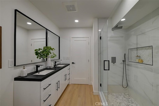 full bath with a marble finish shower, wood finished floors, a sink, and visible vents