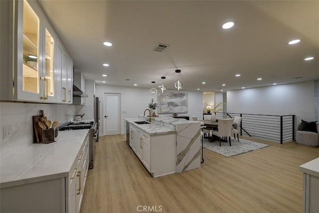 kitchen featuring pendant lighting, white cabinets, a center island with sink, and light hardwood / wood-style flooring